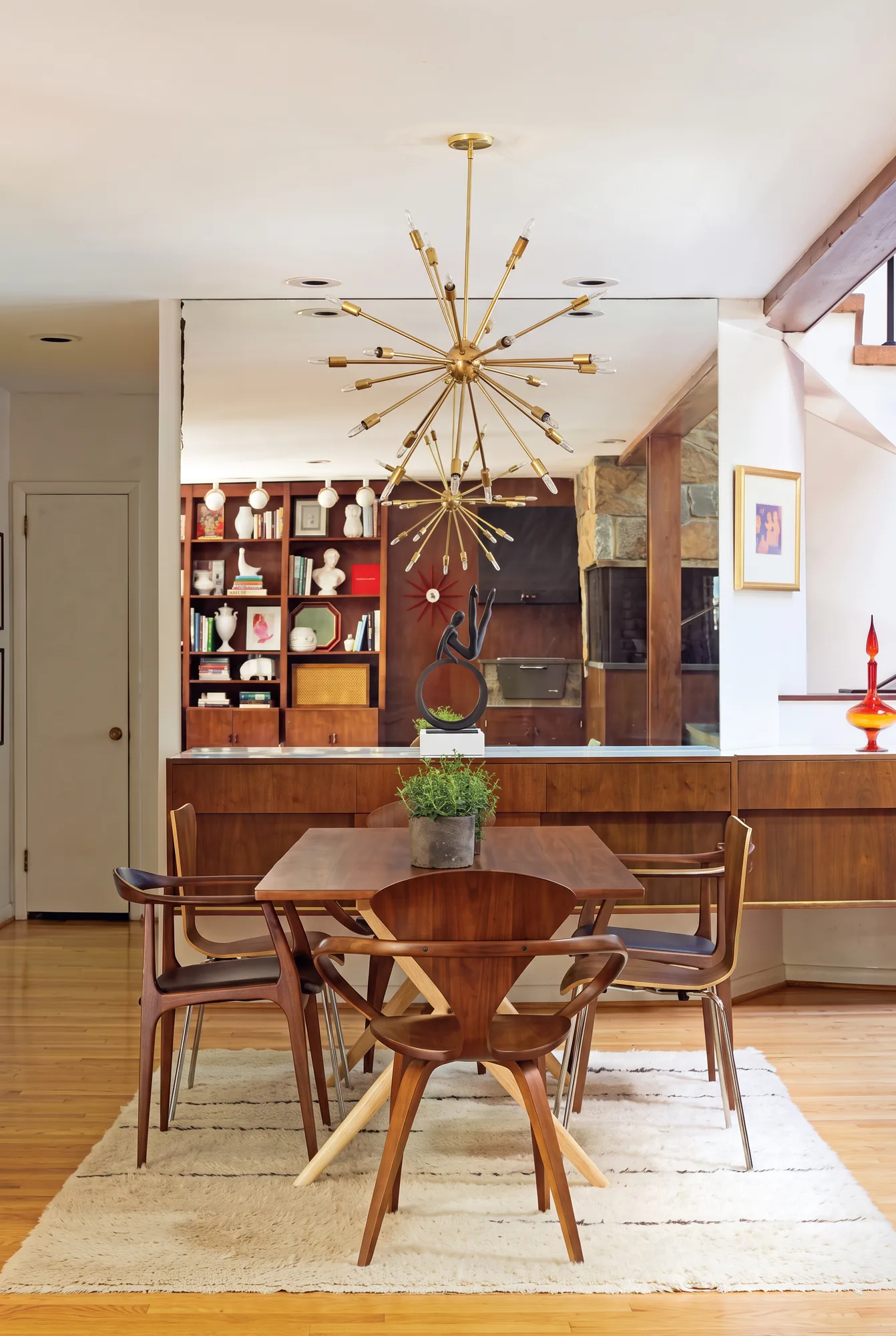 A mid-century dining room with a walnut credenza, walnut armchairs around a walnut table, and a brass sputnik chandelier overhead