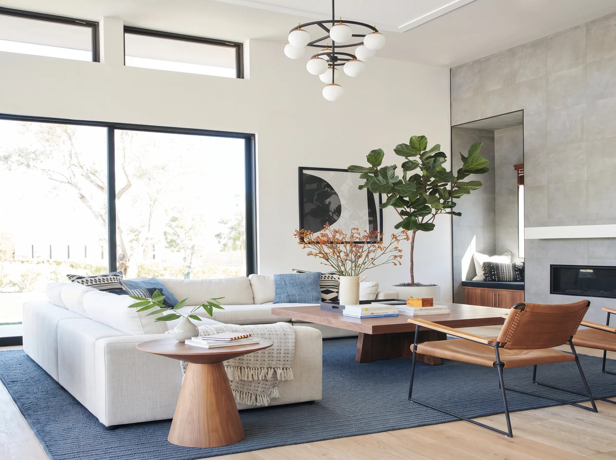 A bright living room with a white sectional sofa, tan leather chairs, a blue wool rug and a low walnut coffee table on a pale oak floor.