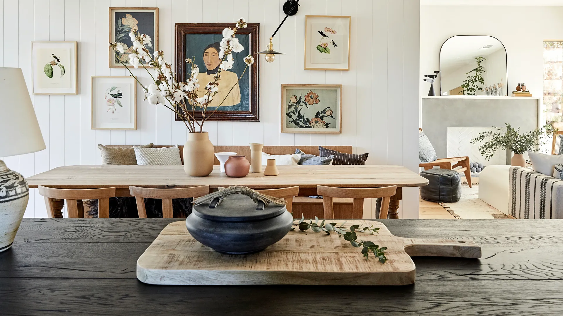 Japandi dining room with a pale oak table and chairs, a gallery wall of framed botanical prints and a dark oak console in the foreground.