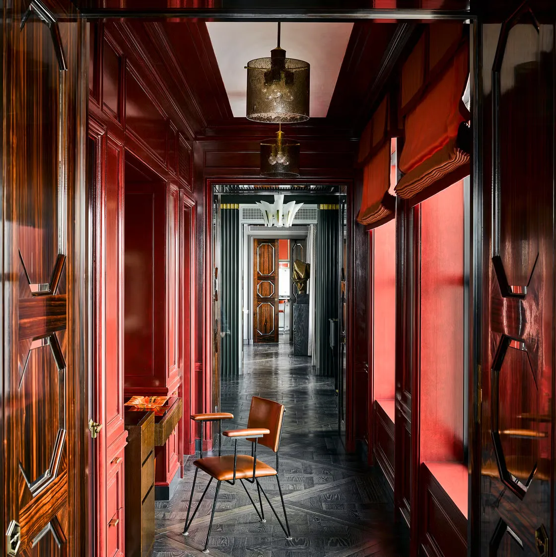 Hallway panelled in high gloss red lacquer with macassar ebony doors, a geometric parquet floor and a bronze mesh pendant.