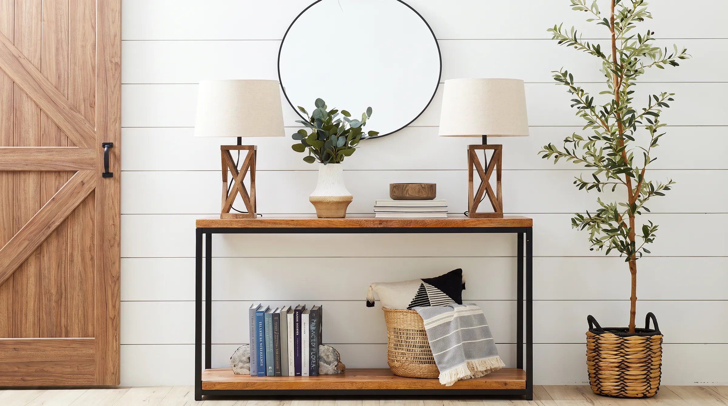 Modern farmhouse entry with a shiplap wall, a round black framed mirror, a wood and black metal console table with two lamps and a sliding timber barn door.