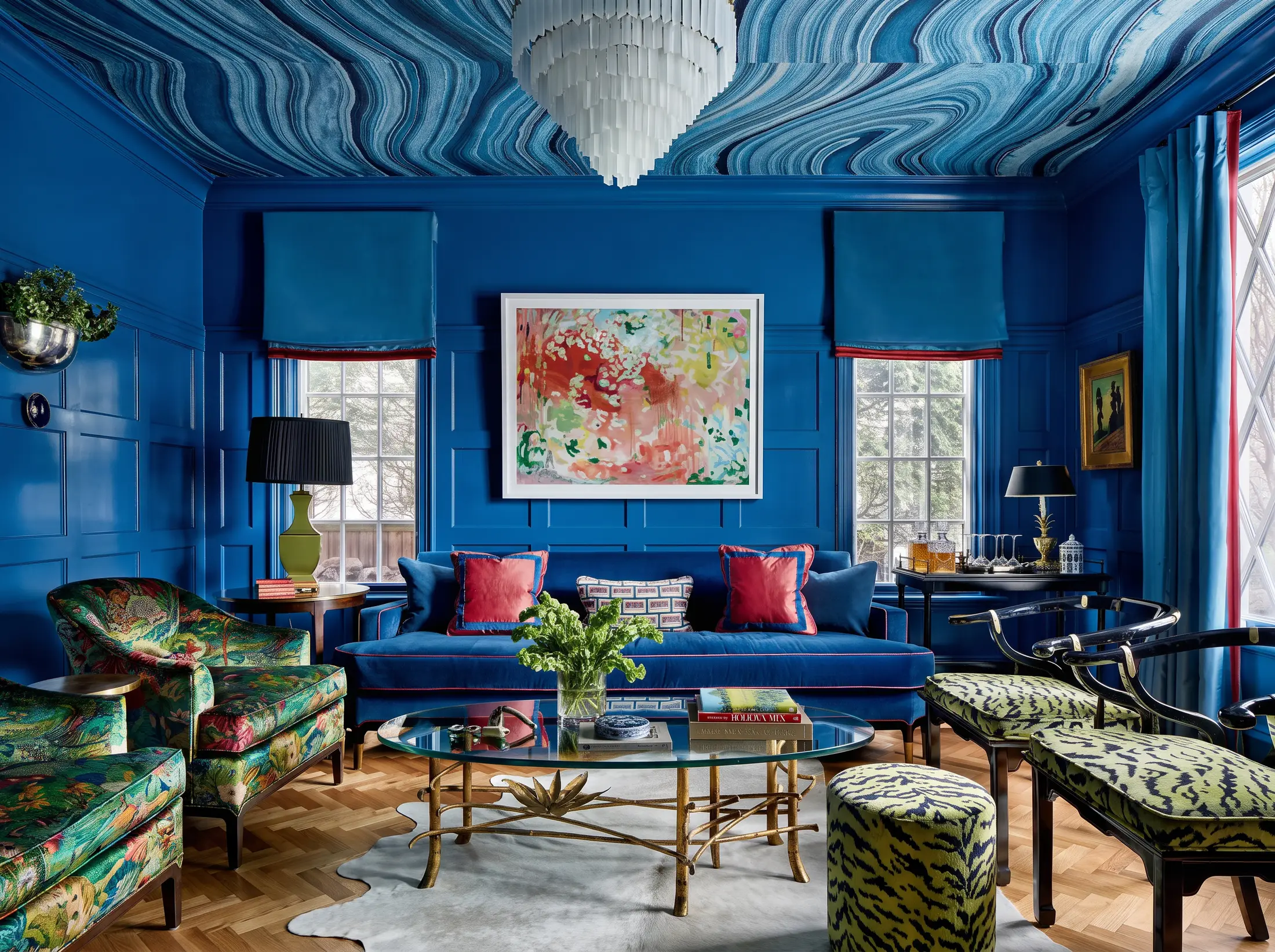 A living room drenched in glossy blue, with a marbled wallpaper ceiling, a blue velvet sofa, floral armchairs and animal print stools.
