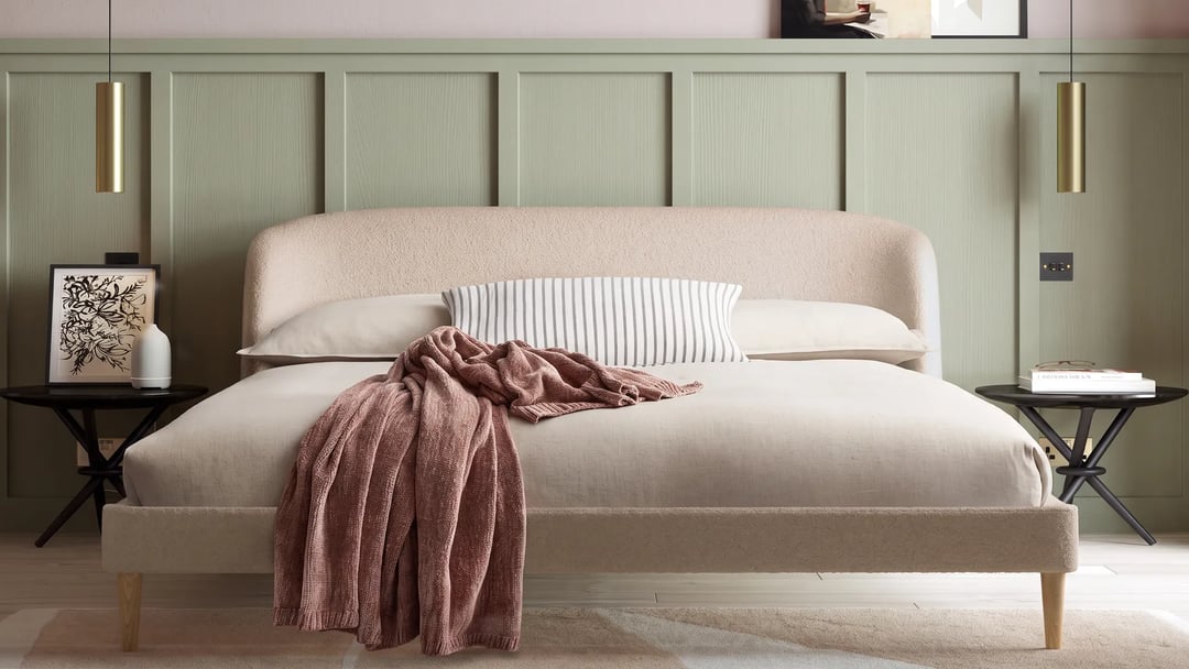 Cream upholstered double bed with a curved headboard and wooden legs against a sage green panelled wall