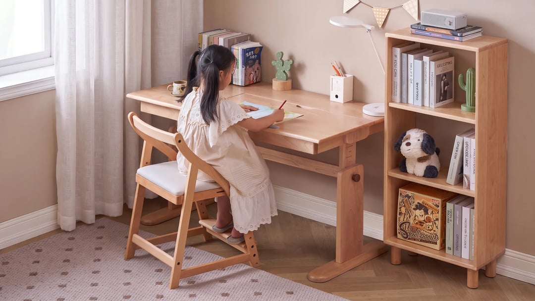 Girl writing at a height-adjustable wooden study desk on a growing wooden chair with a footrest, matching bookcase beside it