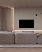 Wall mounted television on a pale plaster wall above a low oak ledge, facing a light grey modular sofa.