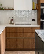 Modern L-shaped kitchen with handleless warm oak fronts, a white worktop, a black island with grey stone and brass pendants.