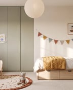 Children's room with a light oak bed with three drawers, a sage green floor-to-ceiling wardrobe and a small desk