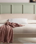 Cream upholstered double bed with a curved headboard and wooden legs against a sage green panelled wall
