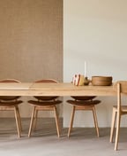 Oak extending dining table opened out, with square corner legs and six wooden chairs in front of a textured wall