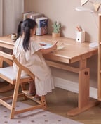 Girl writing at a height-adjustable wooden study desk on a growing wooden chair with a footrest, matching bookcase beside it