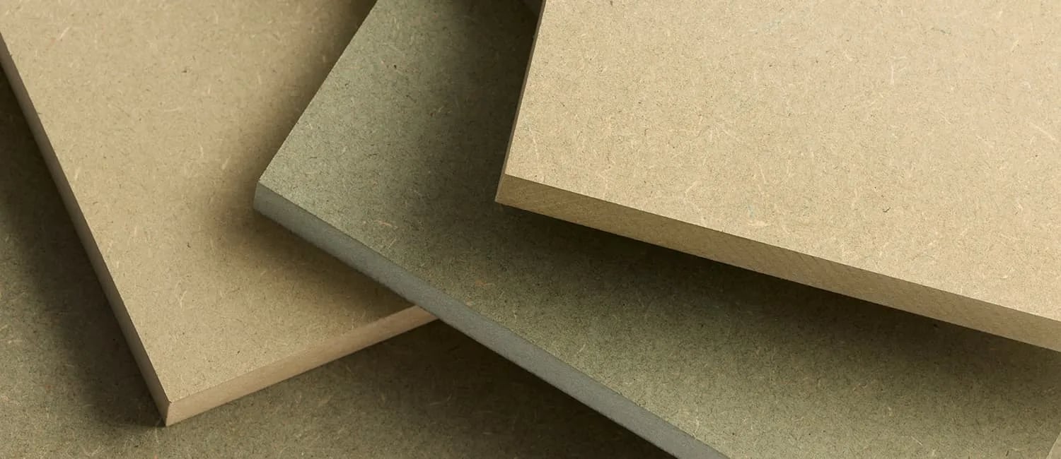 Three raw MDF panels overlapping, two in natural beige and one dyed green to mark it as the moisture-resistant grade.