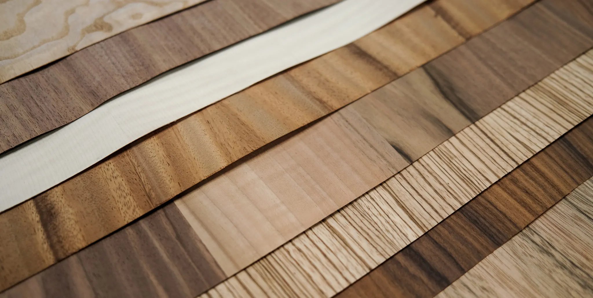 Long sheets of wood veneer laid side by side, showing walnut, oak, maple and pale ash grain.