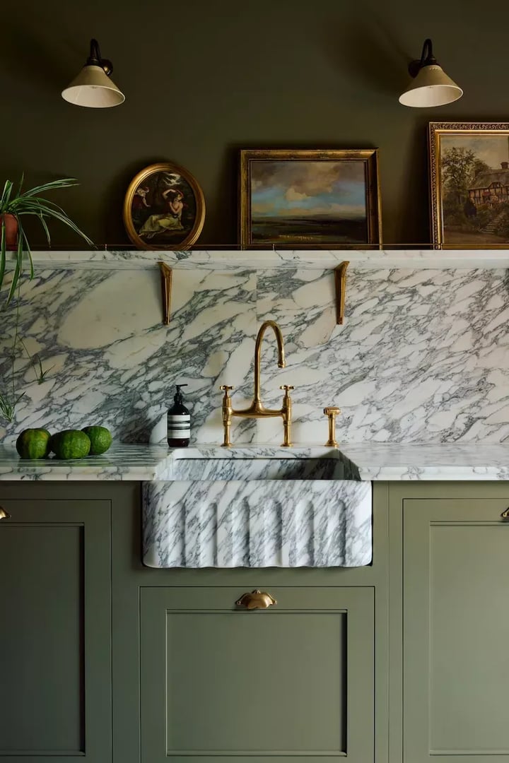 Olive green base units with brass handles, a veined marble sink and splashback, and a dark green wall above.