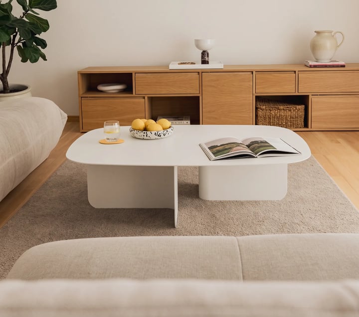 Modern matt white coffee table with a rounded top on two block bases between two beige sofas, an oak sideboard behind