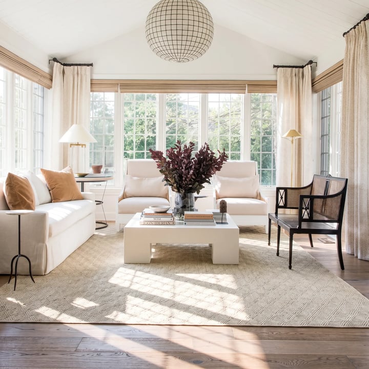 A sunlit sitting room with a cream sofa, ochre cushions, a woven wool rug, linen curtains and three separate light sources.
