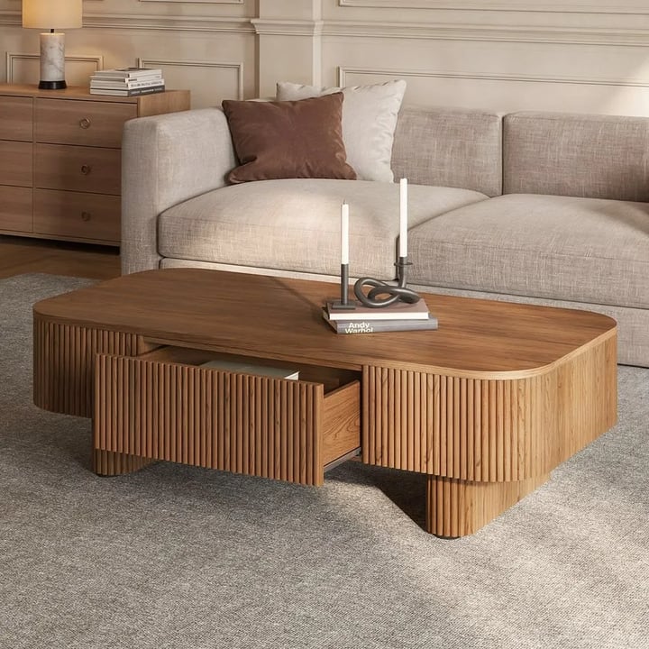 Walnut coffee table with fluted sides and an open drawer, candles and books on top, in front of a beige sofa on a grey rug
