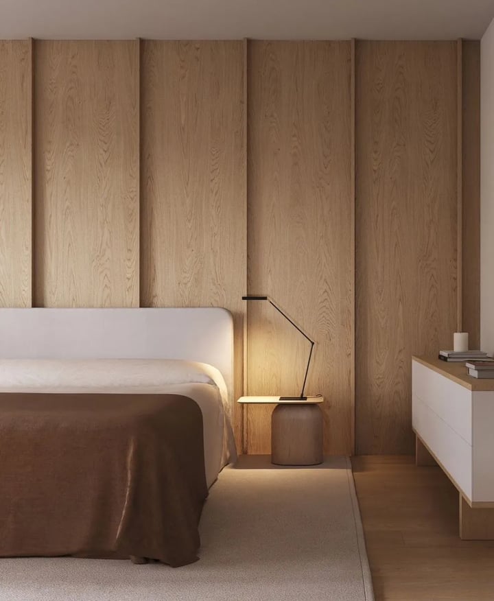 Stool-shaped nightstand beside an upholstered bed with a reading lamp on it, oak-panelled wall