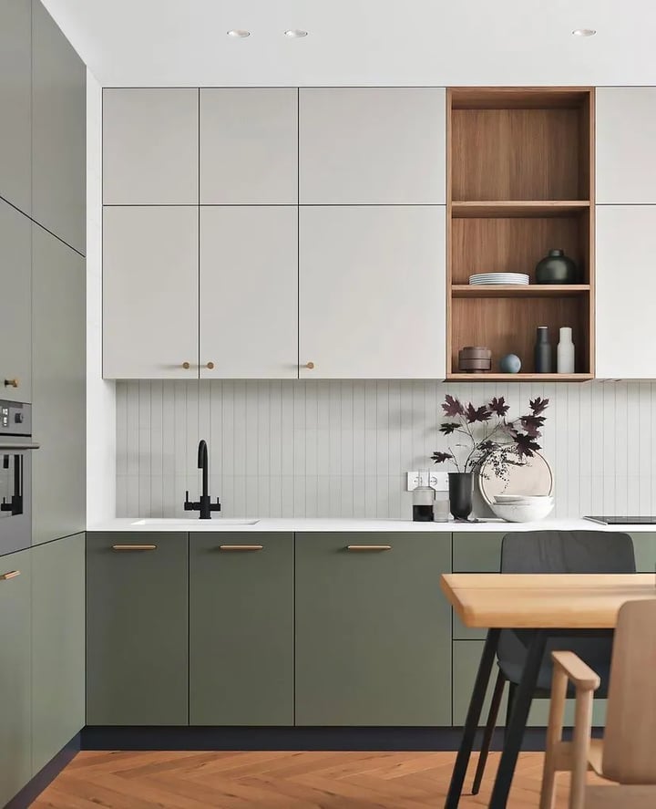 Matt olive green base units with brass handles, warm grey wall cabinets and a walnut open shelf niche.