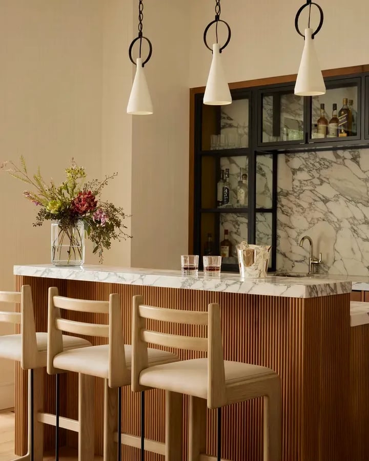 Veined marble counter continuing as a splashback, on a fluted wood base, with oak stools in front.