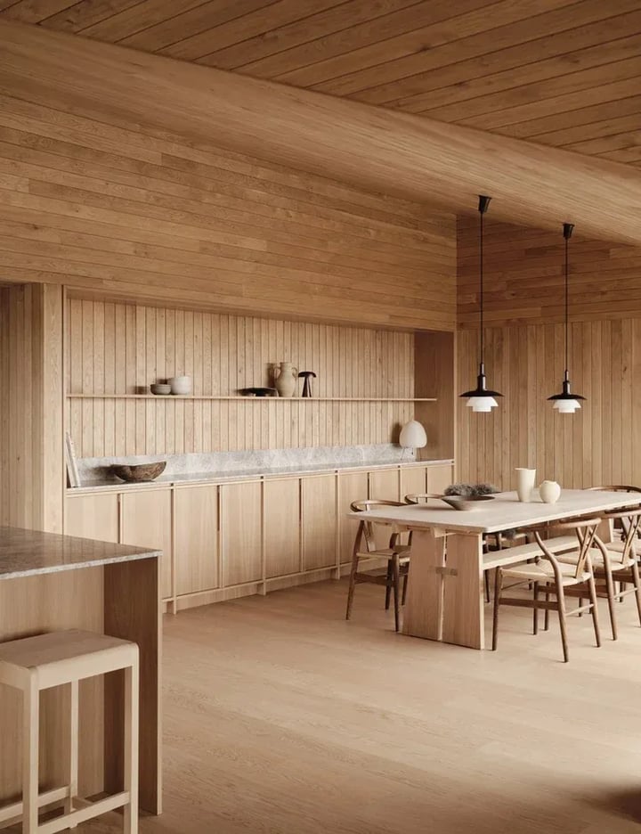 Open-plan oak kitchen with an island worktop in front, a long run of cabinets behind and a dining table under pendants.