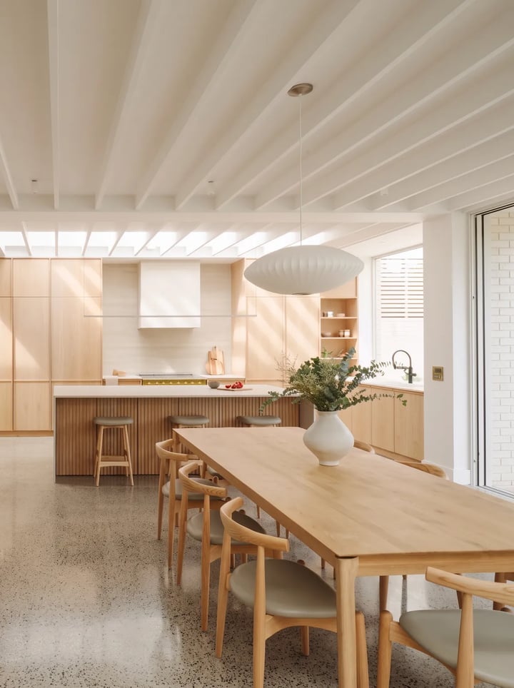 Oak dining table with grey leather chairs in an open plan kitchen, with a clear walkway to a fluted oak island