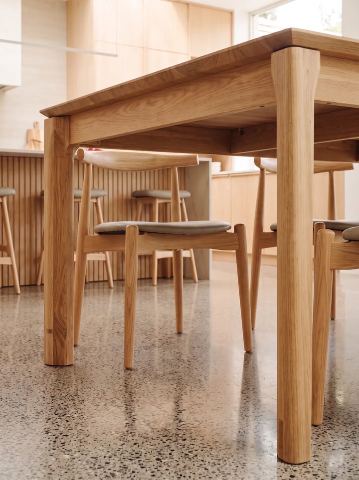 View from below an oak dining table: the apron under the top, a corner leg and a chair seat tucked beneath it