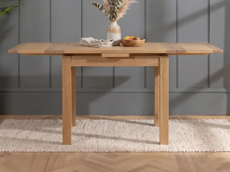 Small oak draw-leaf dining table extended at both ends in front of a grey panelled wall