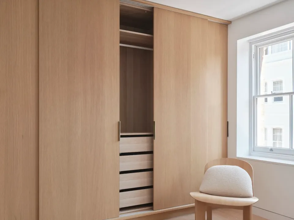 Sliding-door wardrobe with three oak panels in a bedroom, the middle panel open over shelves and drawers