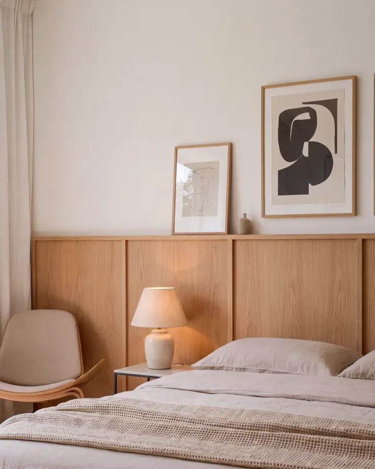 Bed with an oak headboard panel running along the wall, a lamp on a slim nightstand, a chair and two framed prints above