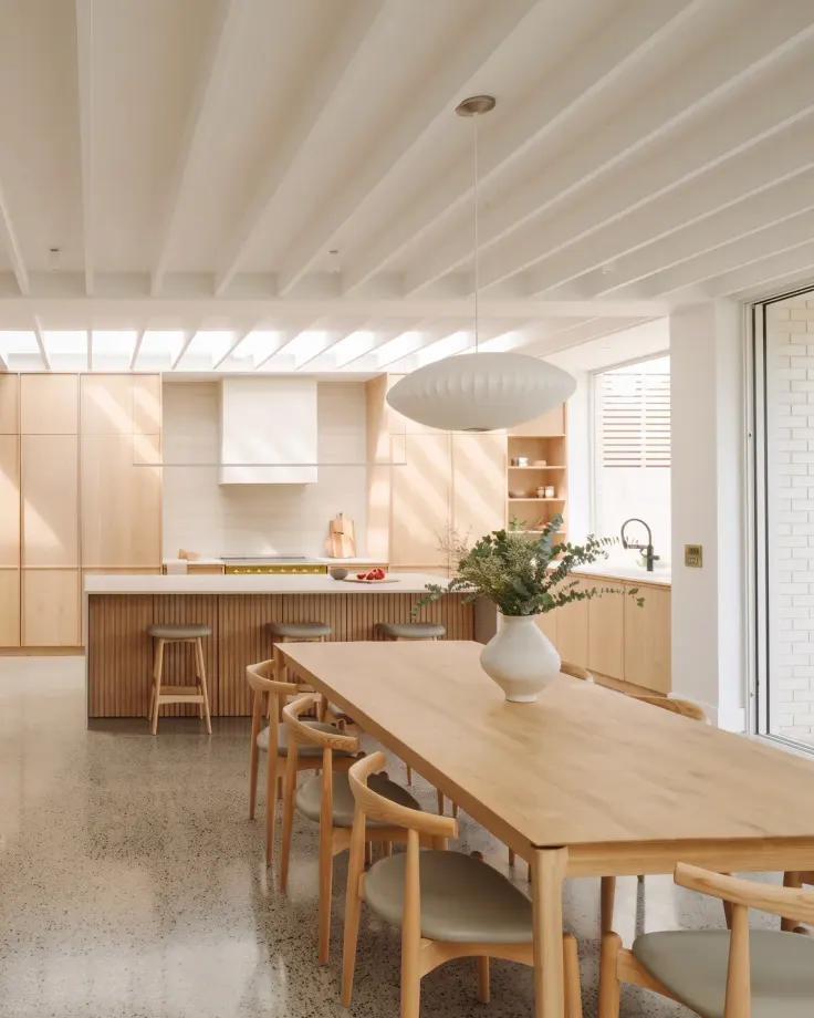 Long solid oak dining table with wishbone chairs in an open-plan kitchen, a fluted oak island behind it